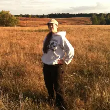 Person with a baseball hat and white sweatshirt standing in a field