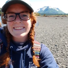 smiling woman wearing glasses and a baseball hat with mountain in background